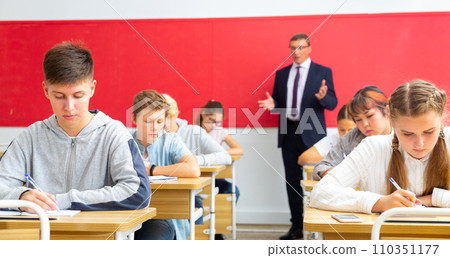 Teenagers listening to lecturer and writing in notebooks in classroom 110351177