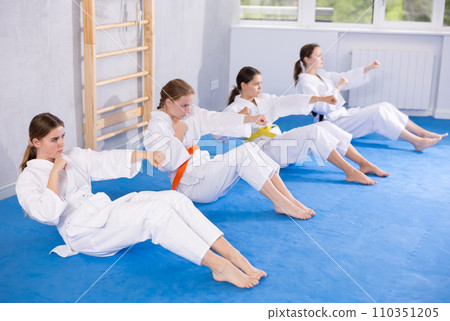Team of teenage girls in kimono train abdominal muscles and do punches at the same time during karate or judo training 110351205