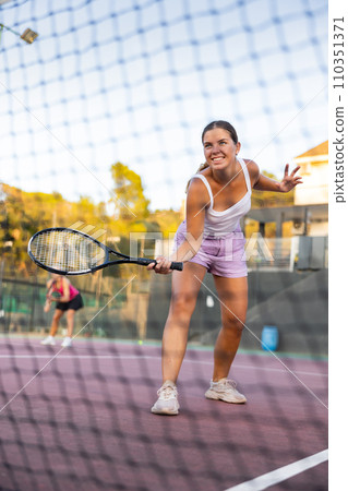 Positive girl in sportswear playing tennis match during training. View through tennis net Positive girl in sportswear playing tennis match during training. View through tennis net 110351371