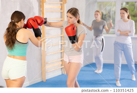 Teen girl in boxing gloves practicing punches in sparring during self-defense course 110351425