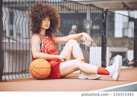 Relaxed, attitude and cool female basketball player relaxing outdoors on a court. Portrait of a trendy and fashionable black woman athlete sitting on the floor with a ball after training 110351485