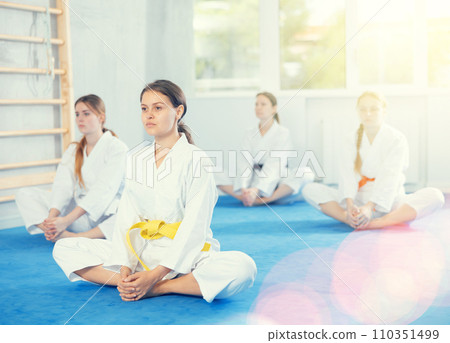 Teenage girl stretching in butterfly pose at group martial arts training Teenage girl stretching in butterfly pose at group martial arts training 110351499