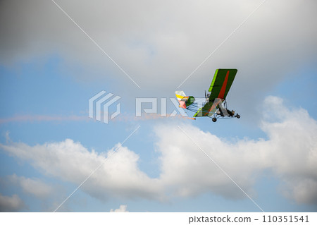 Stunt plane leaves smoke trail in aerobatic performance against blue sky. Skilled pilot maneuvers aeroplane showcasing acrobatic skills and aerial freedom. Stunt plane leaves smoke trail in aerobatic performance against blue sky. Skilled pilot maneuvers aeroplane showcasing acrobatic skills and aerial freedom. 110351541