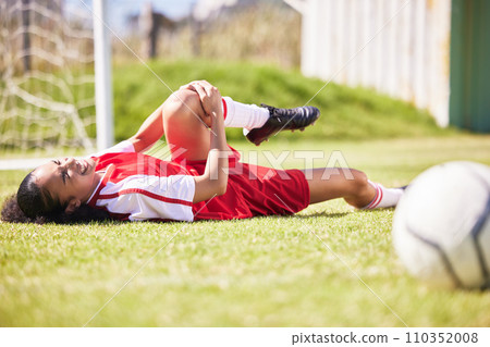 Injured, pain or injury of a female soccer player lying on a field holding her knee during a match. Hurt woman footballer with a painful leg on the ground in agony having a bad day on the pitch 110352008