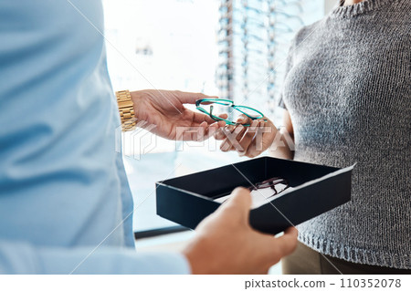 Vision, sight and treatment by an optometrist giving a woman a pair of glasses. Closeup of a female buying spectacles to help with blurry vision. Lady with bad or weak eyesight getting eyeglasses Vision, sight and treatment by an optometrist giving a woman a pair of glasses. Closeup of a female buying spectacles to help with blurry vision. Lady with bad or weak eyesight getting eyeglasses 110352078