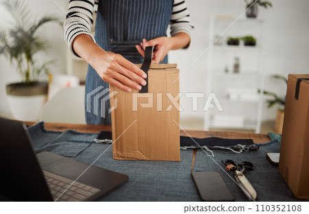 Packing parcel, package and shop order with duct tape while packaging, boxing and wrapping product. Small business tailor hands with laptop and clothing gift for courier shipping, selling or delivery 110352108