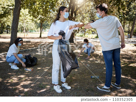 Covid, cleaning and volunteers wearing masks while cleaning a community park and saying thank you with a elbow gesture. Social disdancing between friends doing a cleanup outdoors during a pandemic Covid, cleaning and volunteers wearing masks while cleaning a community park and saying thank you with a elbow gesture. Social disdancing between friends doing a cleanup outdoors during a pandemic 110352305