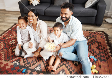 Happy, bonding family quality time at home with parents watching a movie and having snacks on the floor. Young couple being affectionate with their children and enjoying time together indoors 110352868