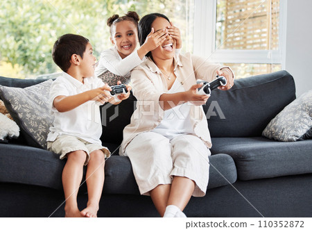 Family, video games and cheating little girl covering her mothers eyes to let her brother win on the couch at home. Entertainment, joystick and having fun while enjoying a bonding activity with kids 110352872