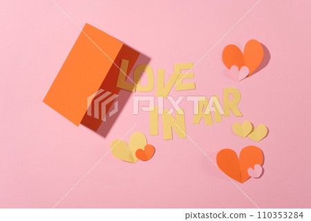 On a pink backdrop, paper hearts, a red card, and the phrase LOVE IN AIR create a romantic ambiance. Ideal for advertising holidays and anniversaries. Flat lay. On a pink backdrop, paper hearts, a red card, and the phrase LOVE IN AIR create a romantic ambiance. Ideal for advertising holidays and anniversaries. Flat lay. 110353284