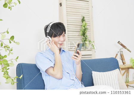 Man listening to music on smartphone at home Man listening to music on smartphone at home 110353361