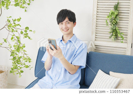 Man using smartphone at home, looking at camera 110353467