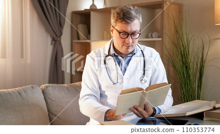 Healthcare studying. Medical knowledge. Smart focused doctor man in clinic white uniform reading book information for professional development at workplace. Healthcare studying. Medical knowledge. Smart focused doctor man in clinic white uniform reading book information for professional development at workplace. 110353774