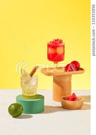 A glass of lemonade and a glass of watermelon juice stand out against a yellow background with some wooden utensils. Fascinating scene. Detoxification of the body concept. A glass of lemonade and a glass of watermelon juice stand out against a yellow background with some wooden utensils. Fascinating scene. Detoxification of the body concept. 110353956