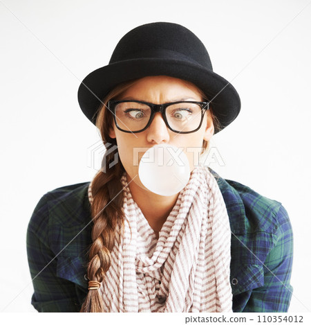 Cool, gum and a woman blowing a bubble for comedy, funny and crazy on a white background. Comic, stylish and a goofy young girl with bubblegum, weird face and quirky on a studio backdrop with glasses 110354012