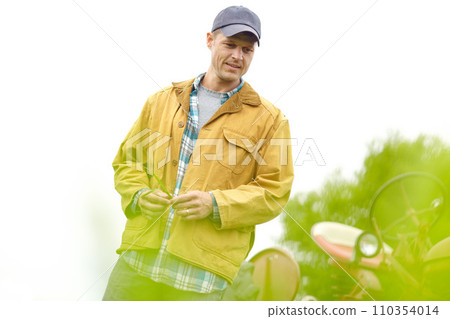 Examing the farmland. a farmer standing in a field with his tractor behind him with copyspace. Examing the farmland. a farmer standing in a field with his tractor behind him with copyspace. 110354014