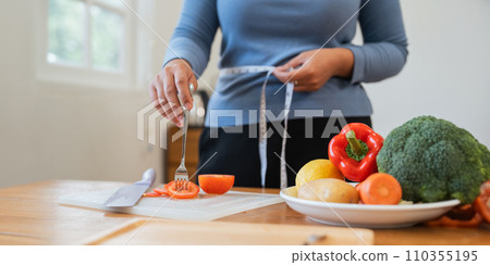 Young woman asian measure her waist in the kitchen the with vegetables and fruits. Concept of healthy eating and dieting 110355195