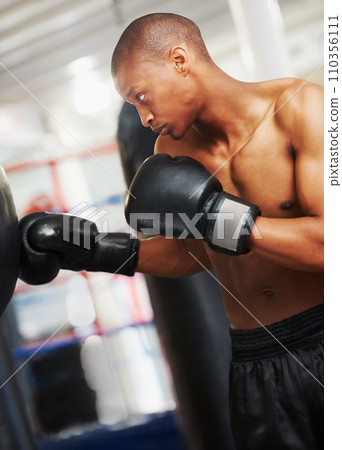 Boxing, gloves and black man training in gym with fitness, power and workout challenge. Strong body, muscle and boxer in club, athlete fighting with bag for exercise and confidence in competition. Boxing, gloves and black man training in gym with fitness, power and workout challenge. Strong body, muscle and boxer in club, athlete fighting with bag for exercise and confidence in competition. 110356111