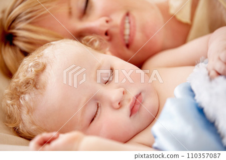 Sleeping, mom and calm baby in bed together with peace, happiness and love for infant in morning nap. Mother, cuddle and sleep with child in closeup and rest with a smile in bedroom or family home 110357087