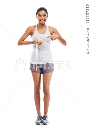 Woman, lose weight and pointing to measuring tape and apple in white background or studio. Indian, model and happy with results of fitness, wellness and diet with healthy food, nutrition and fruit 110357110