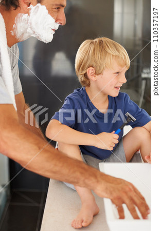 Teaching him manly ways. A young boy sitting on the bathroom sink while his father shaves. 110357197