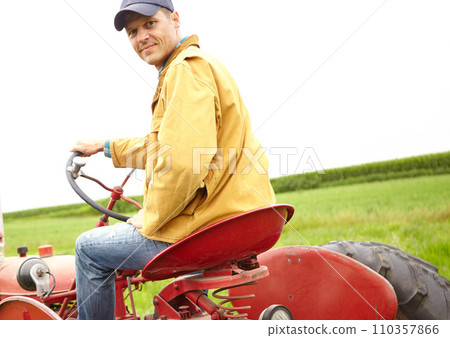 Just an average day at the office. Rearview of a smiling farmer driving his tractor on an open field. 110357866