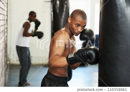 Boxing, gloves and black man training with bag for fitness, power and workout challenge in gym. Strong body, muscle and boxer in club, athlete with exercise and confidence for competition fighting. 110358061