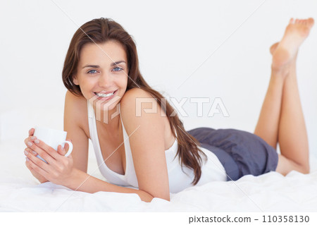 Coffee cup, bed and portrait of happy woman in morning, wake up or natural wellness in home on calm weekend. Relax, drink and peace, smile on face and girl in apartment, bedroom or house with rest. 110358130