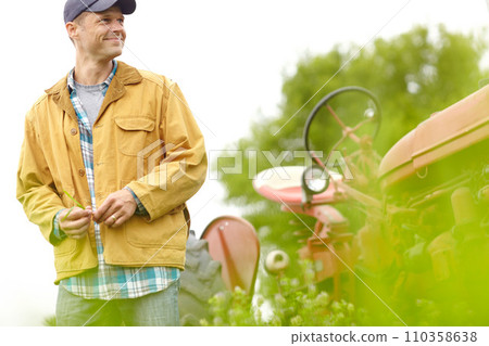 I have a good feeling about this years harvest. a farmer standing next to his tractor and smiling. 110358638