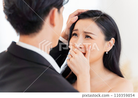 Emotional Asian bride tears up in tender moment with groom at their wedding ceremony. Heartfelt emotions as a woman cries with joy at her wedding. 110359854