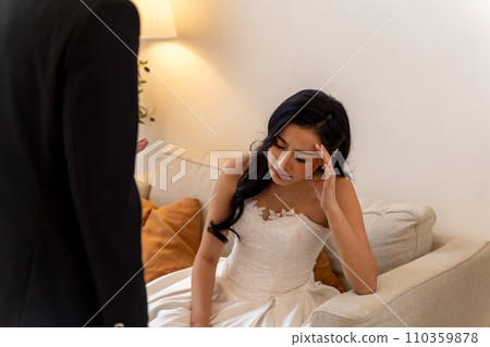 Stressed Asian bride in a heated conversation with groom, a moment of wedding day tension. Elegant wedding dress and formal suit contrast with the conflict between bride and partner 110359878