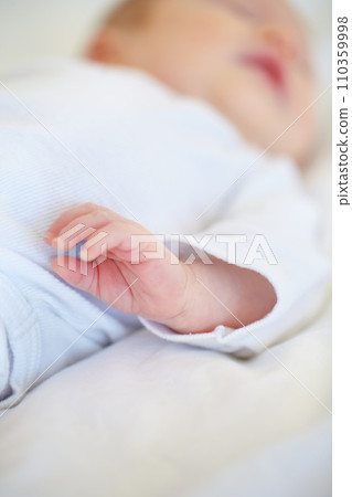 Closeup, baby or new born with hand on bed for love, caring and support in home. Infant, hope and milestone for future, growth or child development with trust for bonding, protection and security 110359998