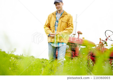 Its just me and my tractor. Portrait of a farmer standing in a field with his tractor parked behind him - Copyspace. 110360003
