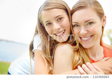 Showing off a family resemblance. A happy young daughter embracing her mother while outdoors. 110360065