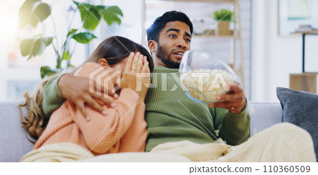 Fear, jump and couple watching tv on a sofa with popcorn for movie, film or streaming show at home. Omg, television and people hug in living room with cinema snack for scary, horror or spooky series 110360509