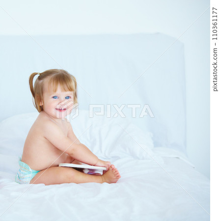 Smile, learning and a baby with a book in the bedroom of a home for growth or child development. Kids, storytelling or reading with a happy young infant girl sitting on a bed in an apartment 110361177