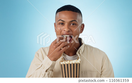 Portrait, happy man and popcorn for cinema in studio on blue background for entertainment mockup. Male model, eating and hungry with delicious, snack and food for watching, television and theatre 110361359