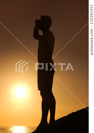 Silhouette, man or looking with hands for view, scenery and wellness on beach with sunset and peace. Person, shadow or adventure and relax for holiday, vacation or experience by ocean or sea with sun 110361951