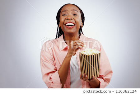 Portrait, laughing or black woman watching a movie in studio for cinema with popcorn to relax. Comedy, funny or happy African person eating snack for streaming film or subscription on grey background 110362124