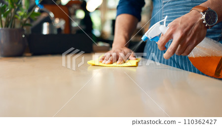 Waiter, hands and cleaning table in restaurant for dust, bacteria and dirt with cloth, spray or detergent. Barista, person or wipe wooden furniture in coffee shop or cafe with chemical liquid closeup 110362427