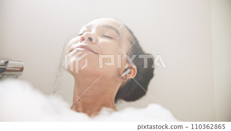 Music, face or happy woman in a bath in hotel cleaning, grooming or body care in soap foam. Relax, earphones or calm lady lying in water in spa, home or bathroom streaming or listening to radio song 110362865