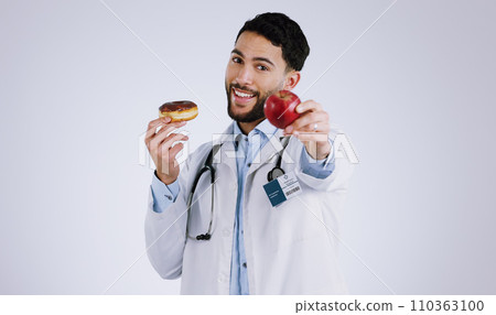 Man, doctor and smile for apple in portrait, choice and donut or snack options in studio mockup. Happy person, nutritionist and healthy food or approval, advice and opinion or diet by gray background 110363100