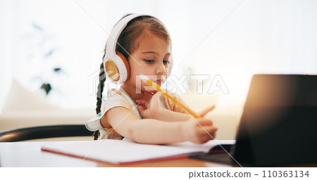 Girl, headphones and writing in book for elearning, education or study on desk at home. Female person, little child or kid taking notes with tablet, headset or technology for virtual class at house 110363134