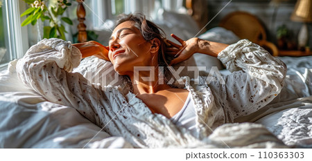 Adult woman stretching in bed waking up in the morning in the sun, World Sleep Day concept Adult woman stretching in bed waking up in the morning in the sun, World Sleep Day concept 110363303
