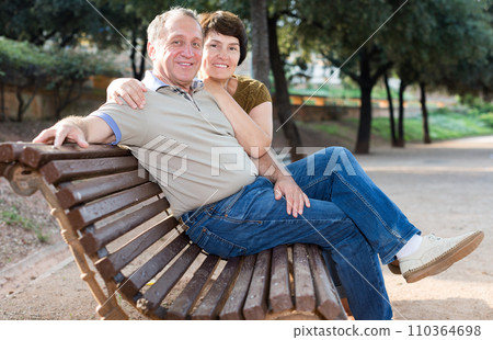 Middleaged male and female posing on bench Middleaged male and female posing on bench 110364698