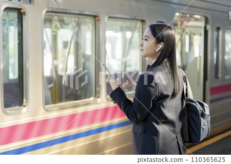 Image of a high school girl commuting to school by train wearing earphones and holding a smartphone 110365625