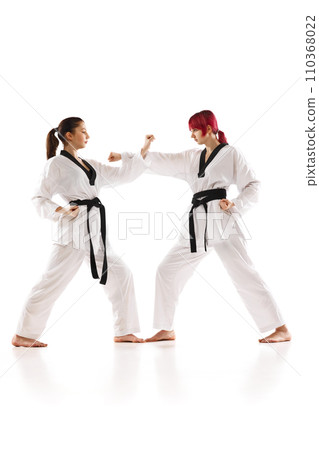 Young sportive girls in kimono and black belted practicing karate, judo, taekwondo stunts isolated over white background 110368022
