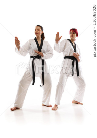 Full-length images of young girls in kimono and black belts, karate, taekwondo, judo athletes standing in poses isolated over white background 110368026