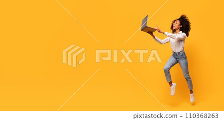 Joyful black woman jumping with laptop on yellow backdrop, panorama with free space Joyful black woman jumping with laptop on yellow backdrop, panorama with free space 110368263