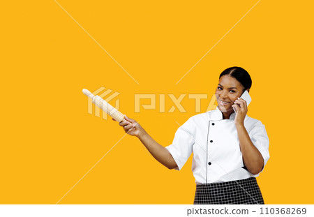 Black female chef making phone call and pointing aside with rolling pin 110368269